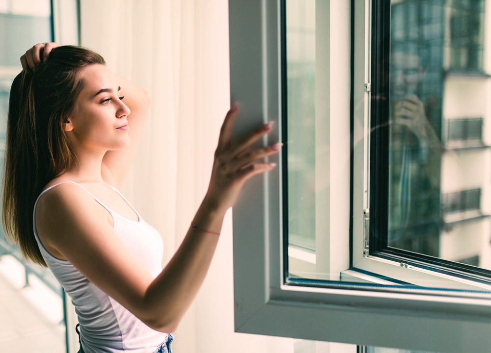 Donna apre una finestra con doppio vetro in un appartamento moderno, godendo della luce naturale e dell’isolamento termico.