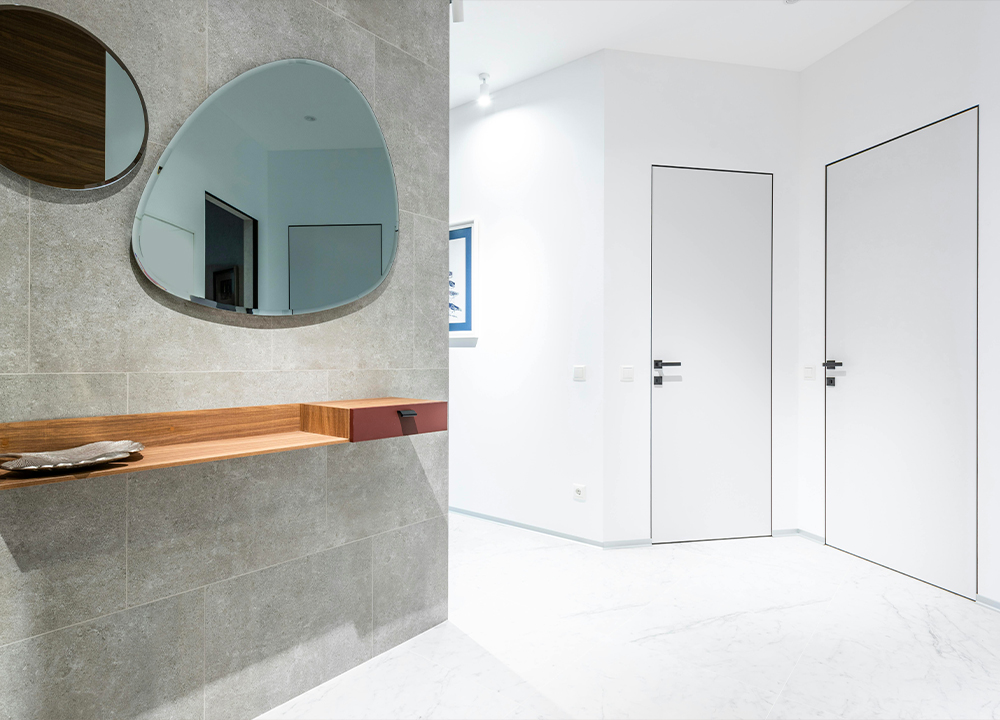 Porte interne bianche filo muro con maniglie nere minimali, inserite in ambiente moderno con pareti chiare e finitura opaca.
