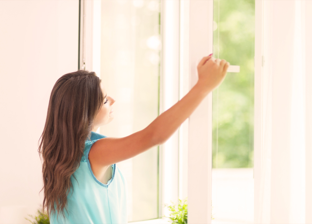 Donna apre una finestra in PVC con doppio vetro durante il giorno, luce naturale e ambiente luminoso, concetto di isolamento termico e risparmio energetico in casa.