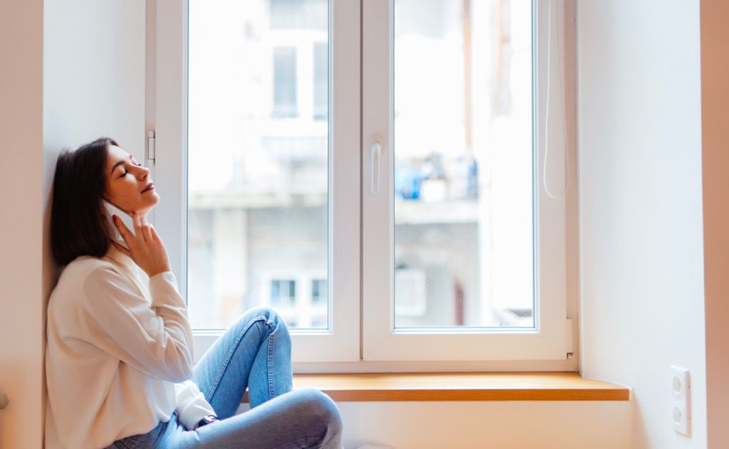 Donna seduta sul davanzale accanto a una finestra in PVC, mentre parla al telefono