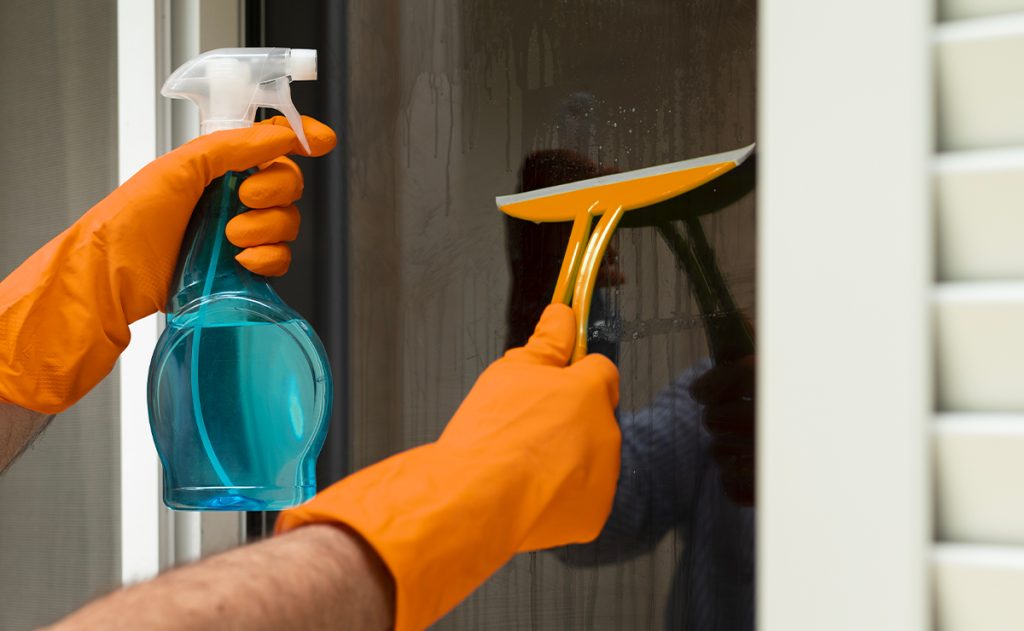 Mani con guanti arancioni che puliscono un vetro basso emissivo