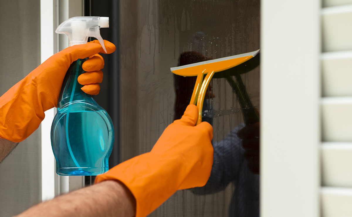 Mani con guanti arancioni che puliscono un vetro basso emissivo