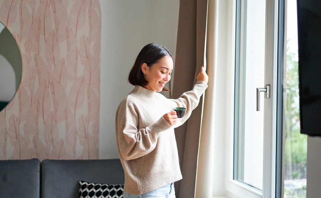 Donna che apre le tende accanto a una finestra moderna con infissi in alluminio dotati di sistemi di sicurezza avanzati.