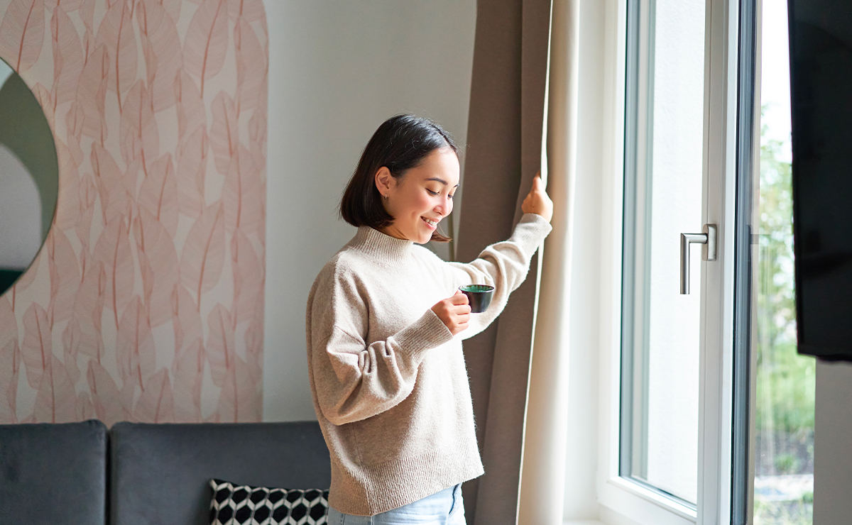 Donna che apre le tende accanto a una finestra moderna con infissi in alluminio dotati di sistemi di sicurezza avanzati.