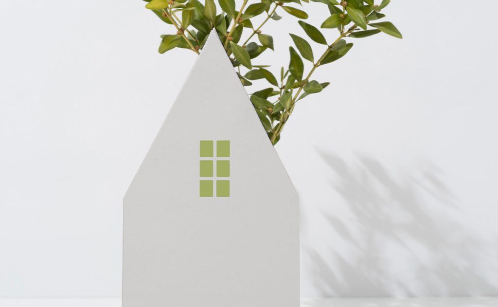 Sagoma bianca a forma di casa con piccole finestre verdi e ramo di foglie sullo sfondo