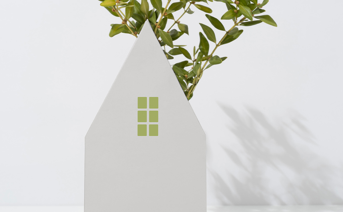 Sagoma bianca a forma di casa con piccole finestre verdi e ramo di foglie sullo sfondo