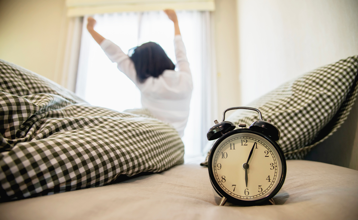 Sveglia su un letto con persona che si stiracchia davanti alla finestra illuminata