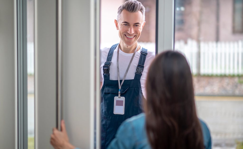 Tecnico degli infissi che sorride alla cliente sulla soglia mentre controlla una finestra