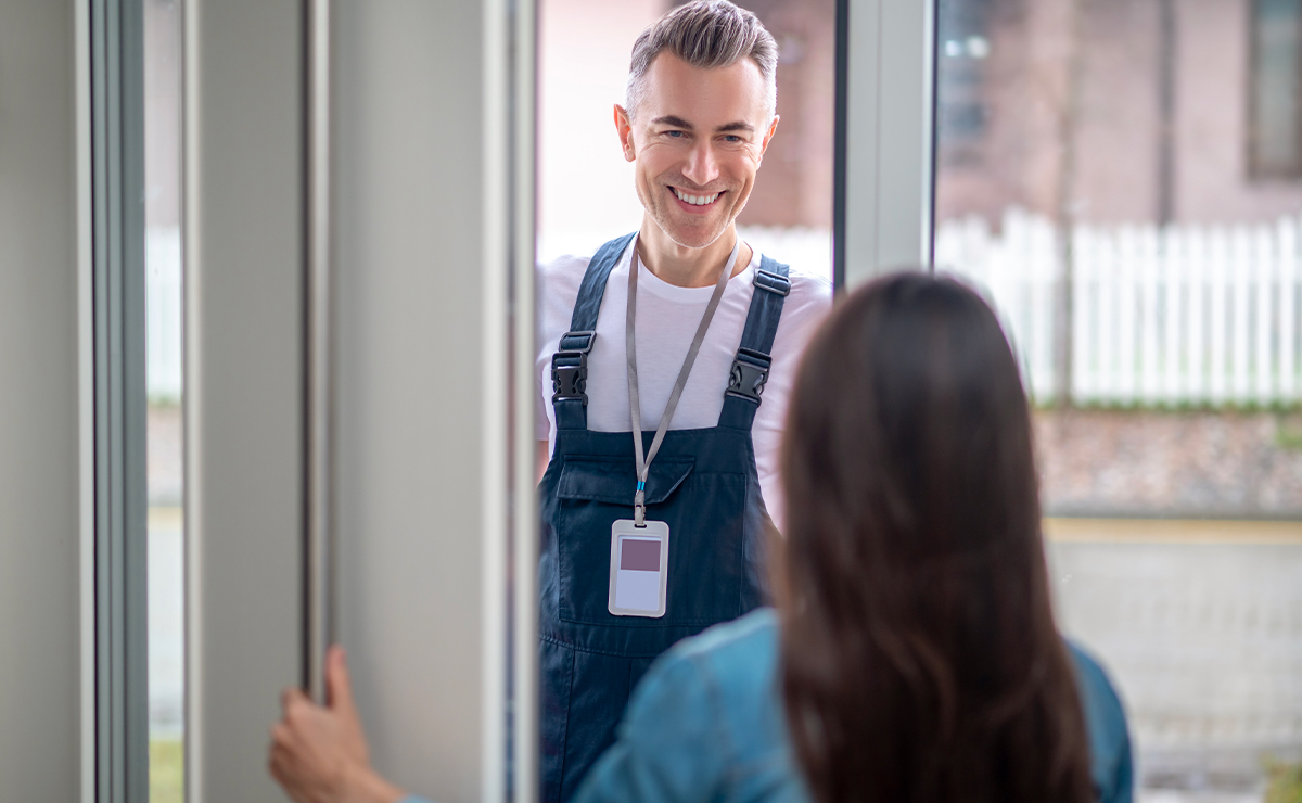 Tecnico degli infissi che sorride alla cliente sulla soglia mentre controlla una finestra